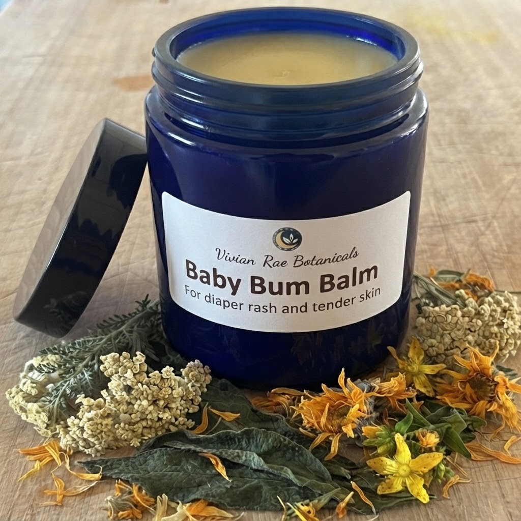 Open blue jar of Baby Bum Balm among yarrow, calendula, comfrey leaves and St. John's wort flowers
