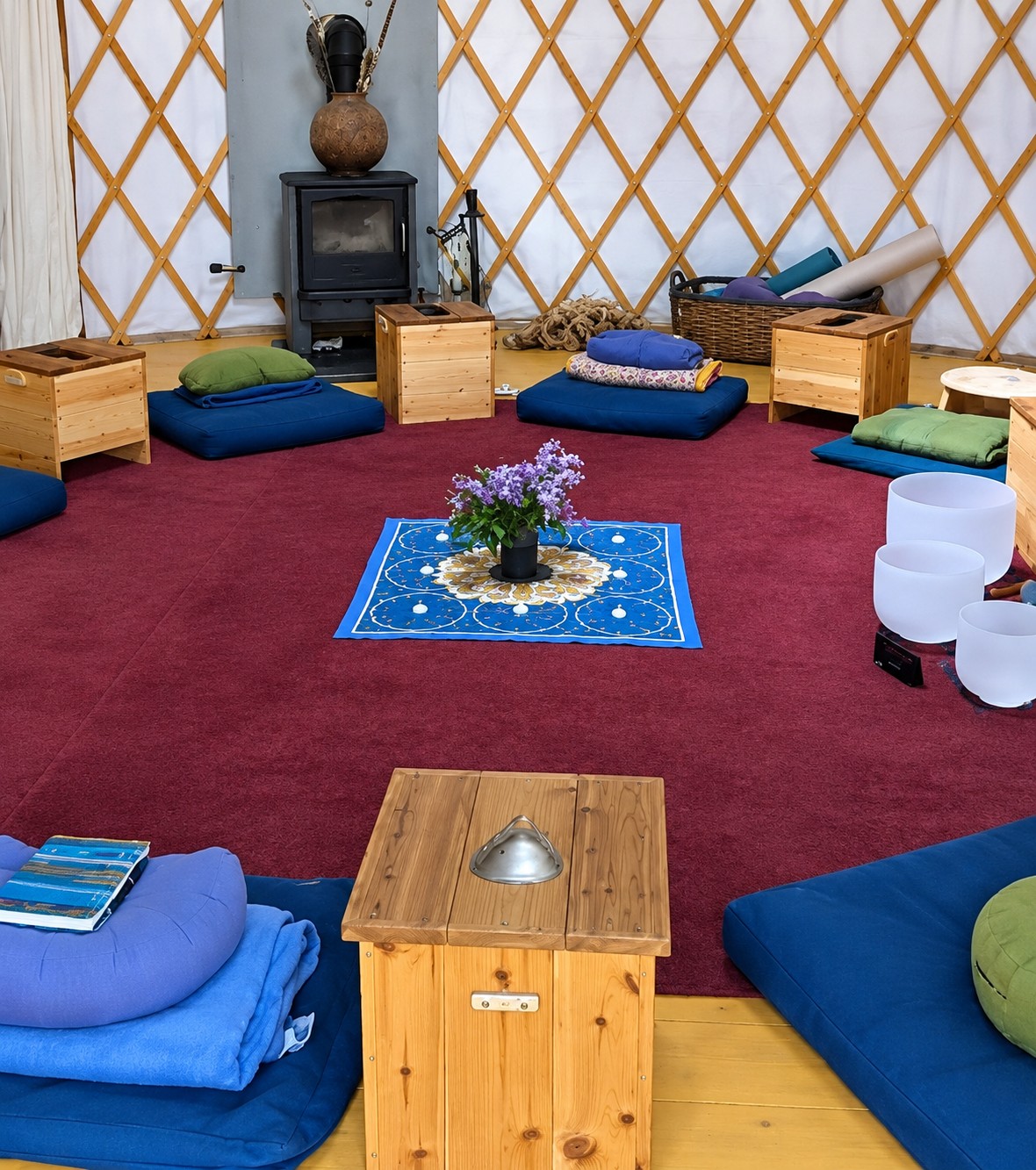 Wooden steam boxes and blue cushions set in a circle inside a yurt, lilacs at the center