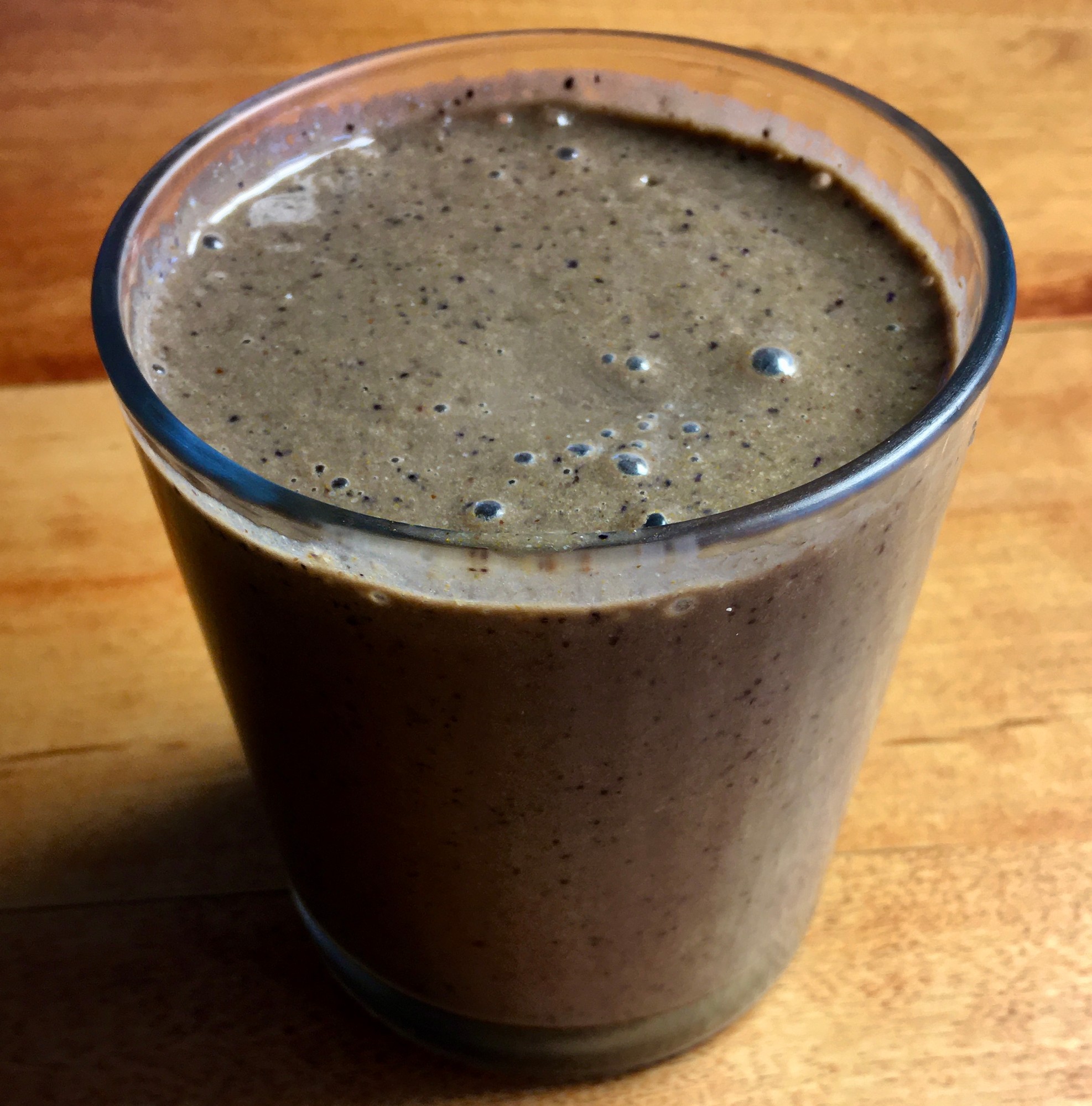 Glass of brown smoothie flecked with dark specks