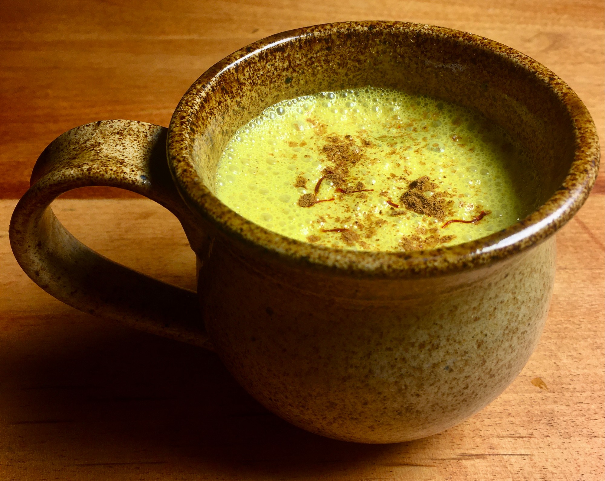 Golden milk sprinkled with cinnamon and saffron threads in a speckled mug