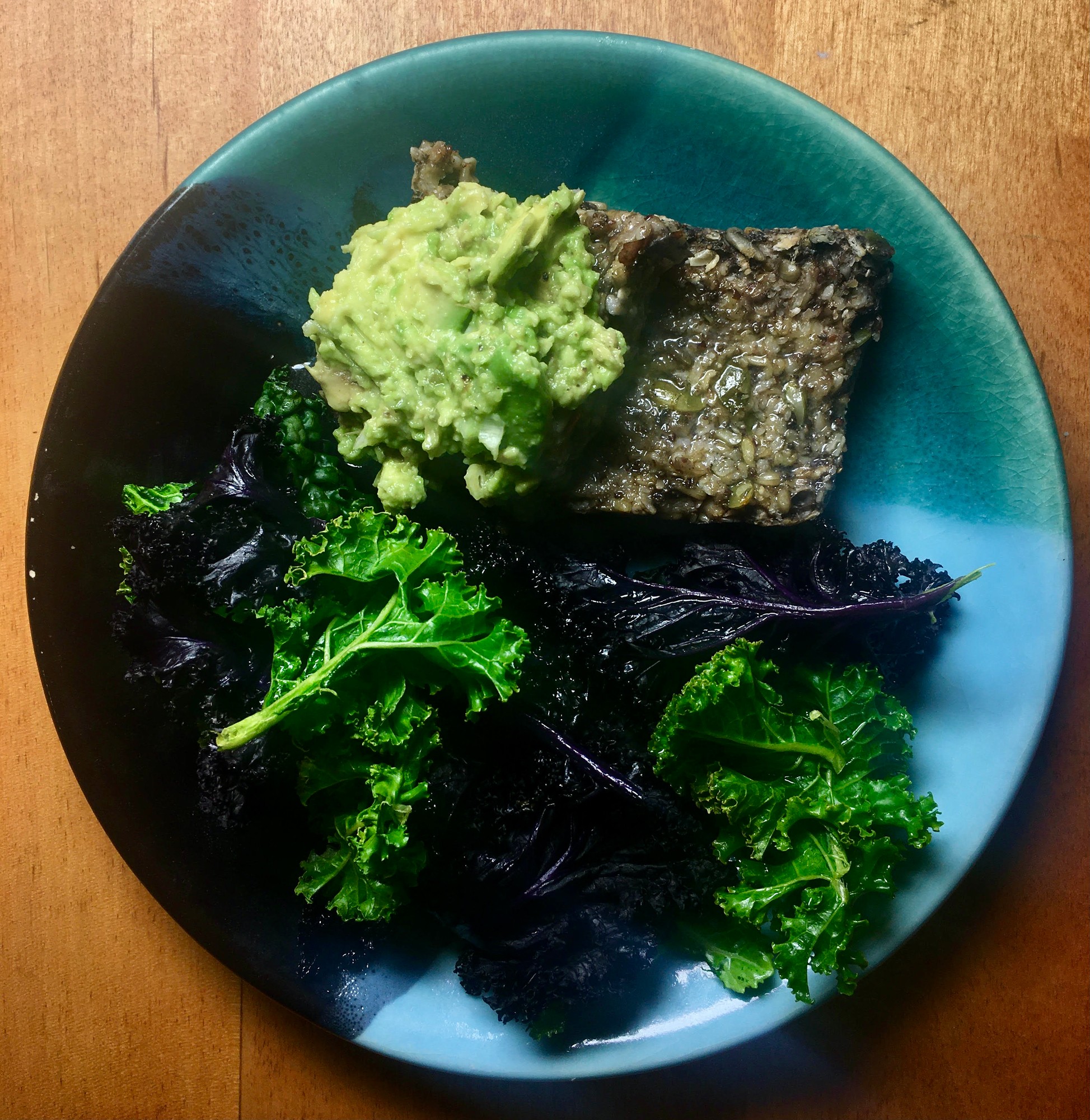 Slice of seed bread with mashed avocado beside green and purple kale