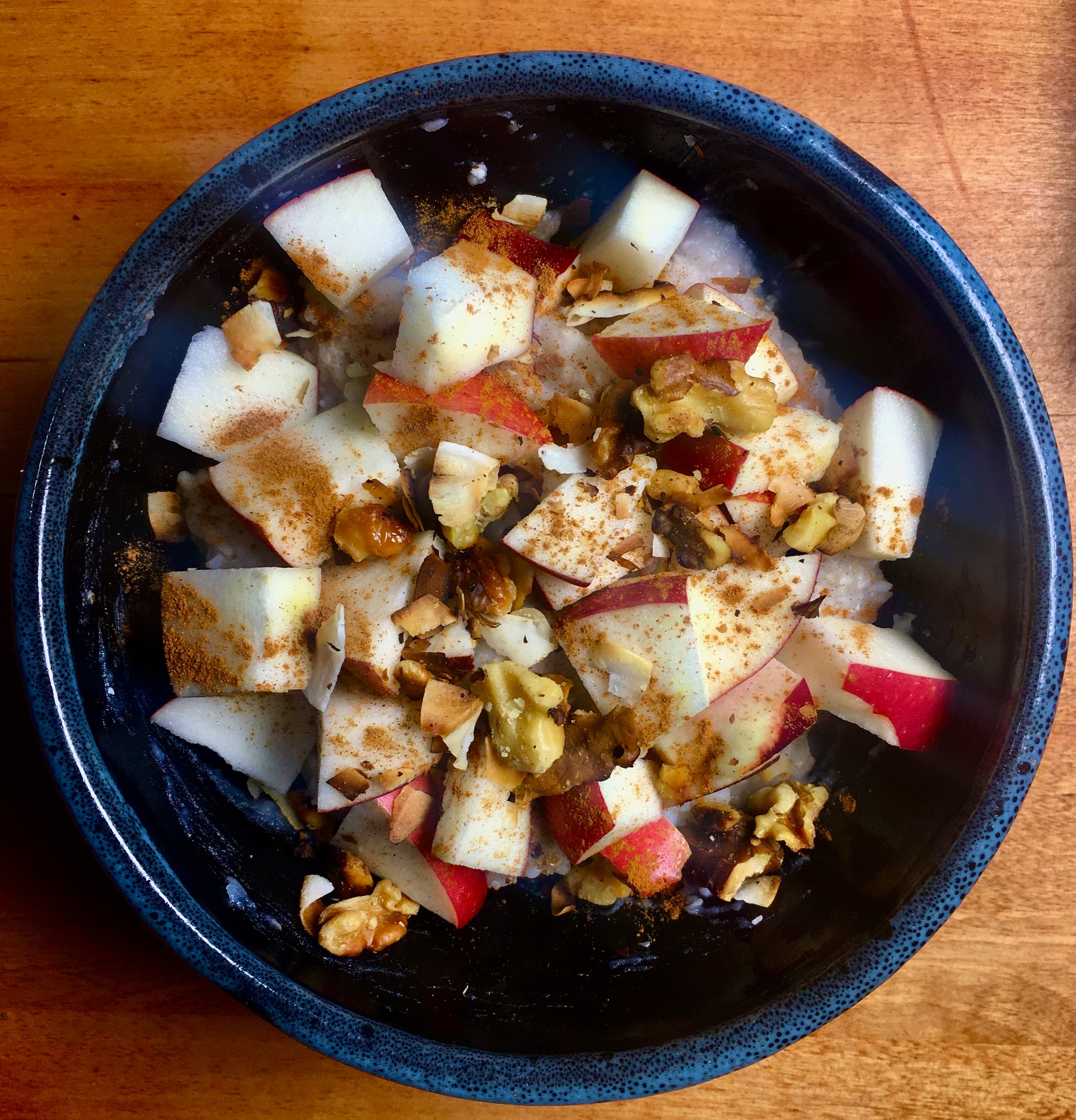 Bowl of oats topped with chopped apple, walnuts, toasted coconut and cinnamon