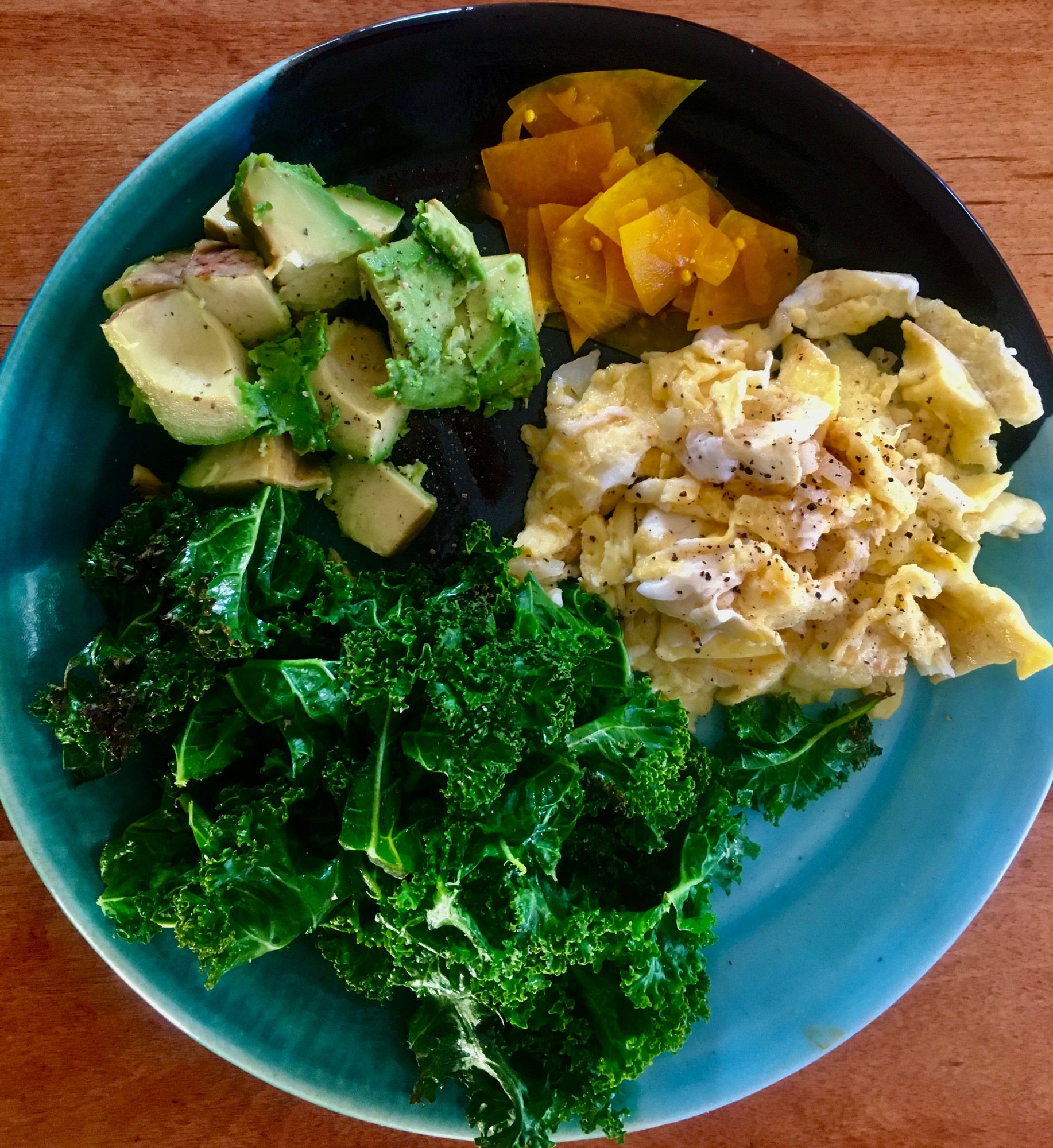 Scrambled eggs with avocado, cooked kale and a yellow pickle on a blue plate