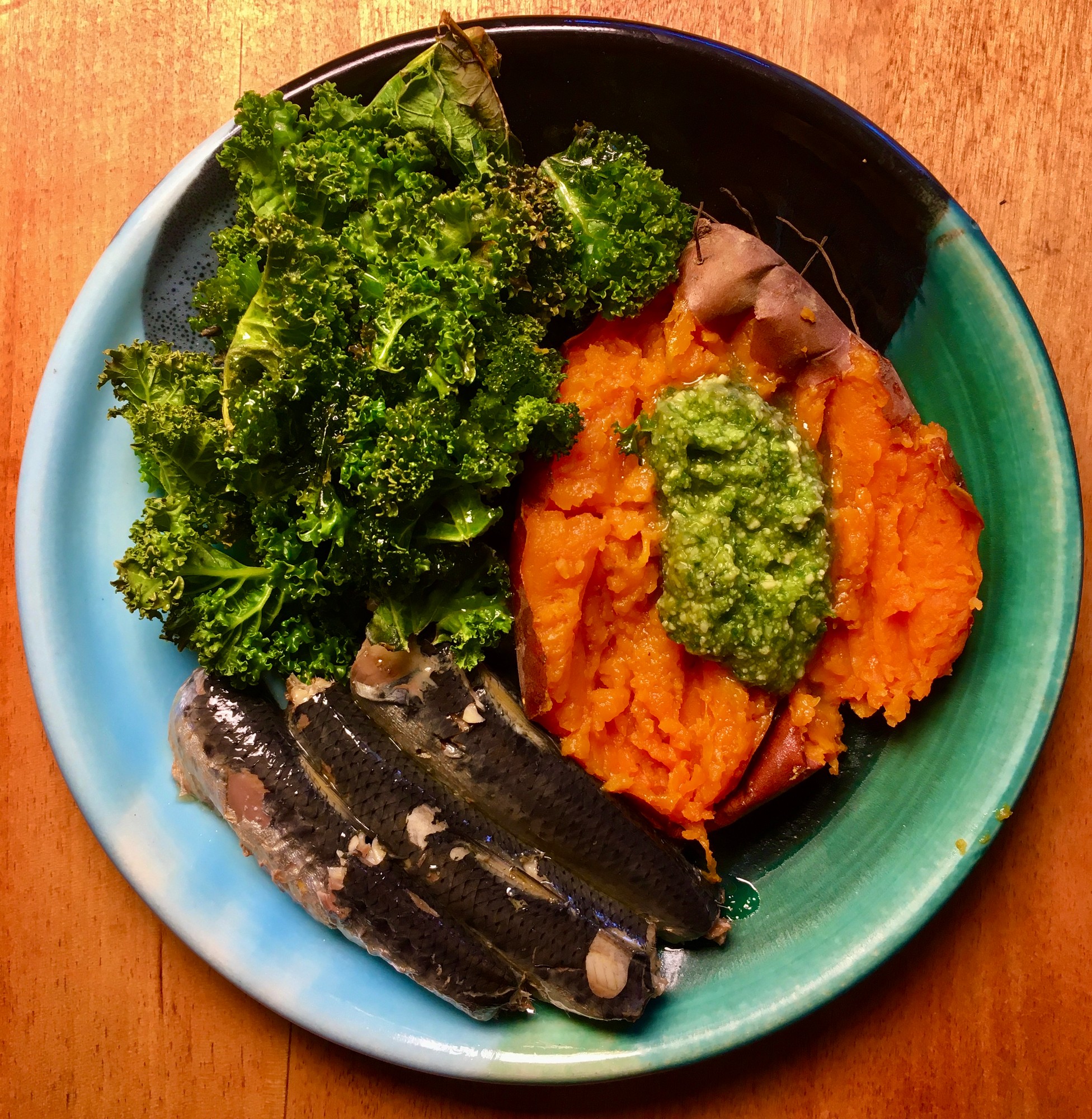 Baked sweet potato topped with pesto beside kale and sardines