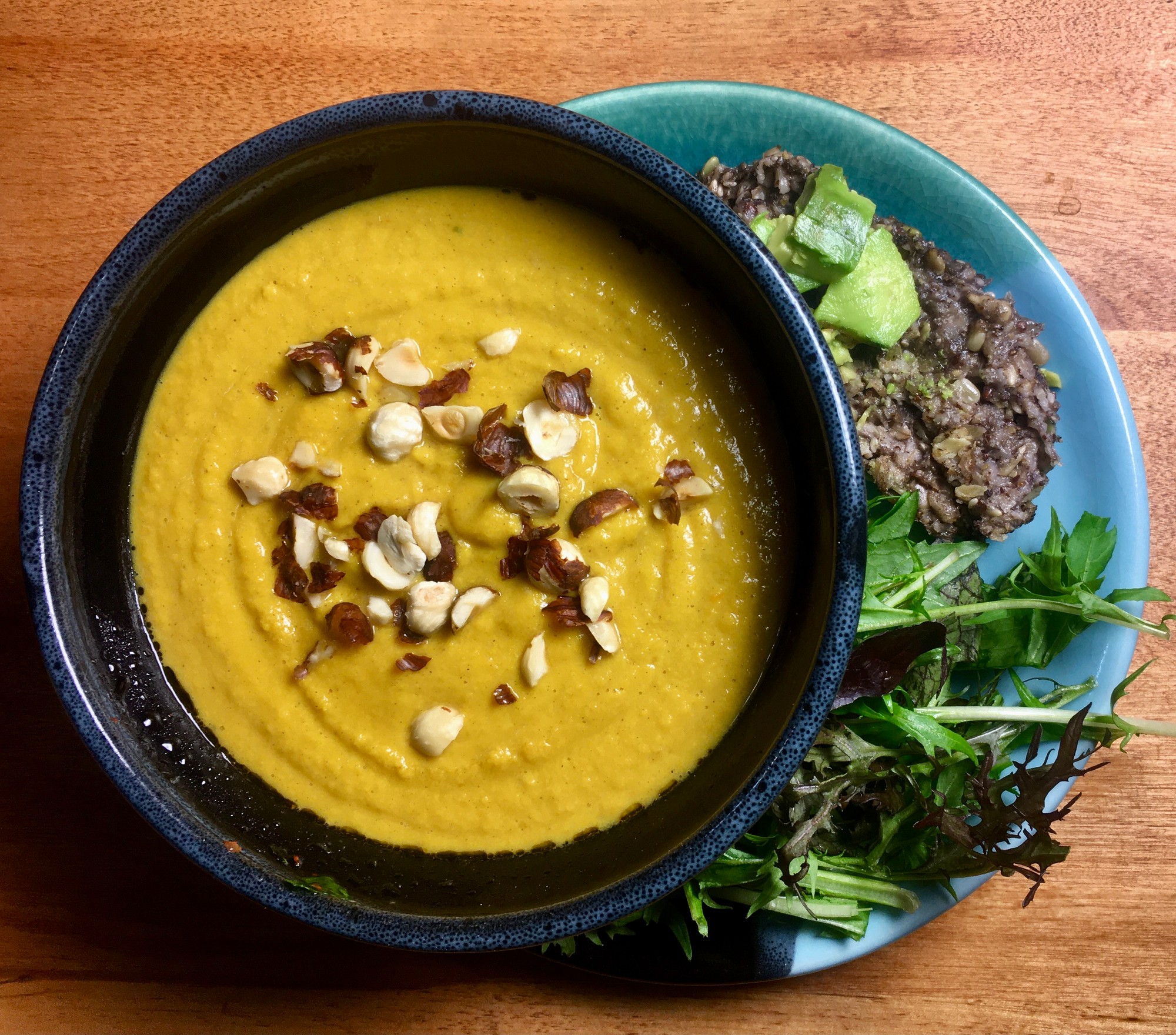 Bowl of butternut squash soup topped with chopped nuts, beside salad and seed bread with avocado