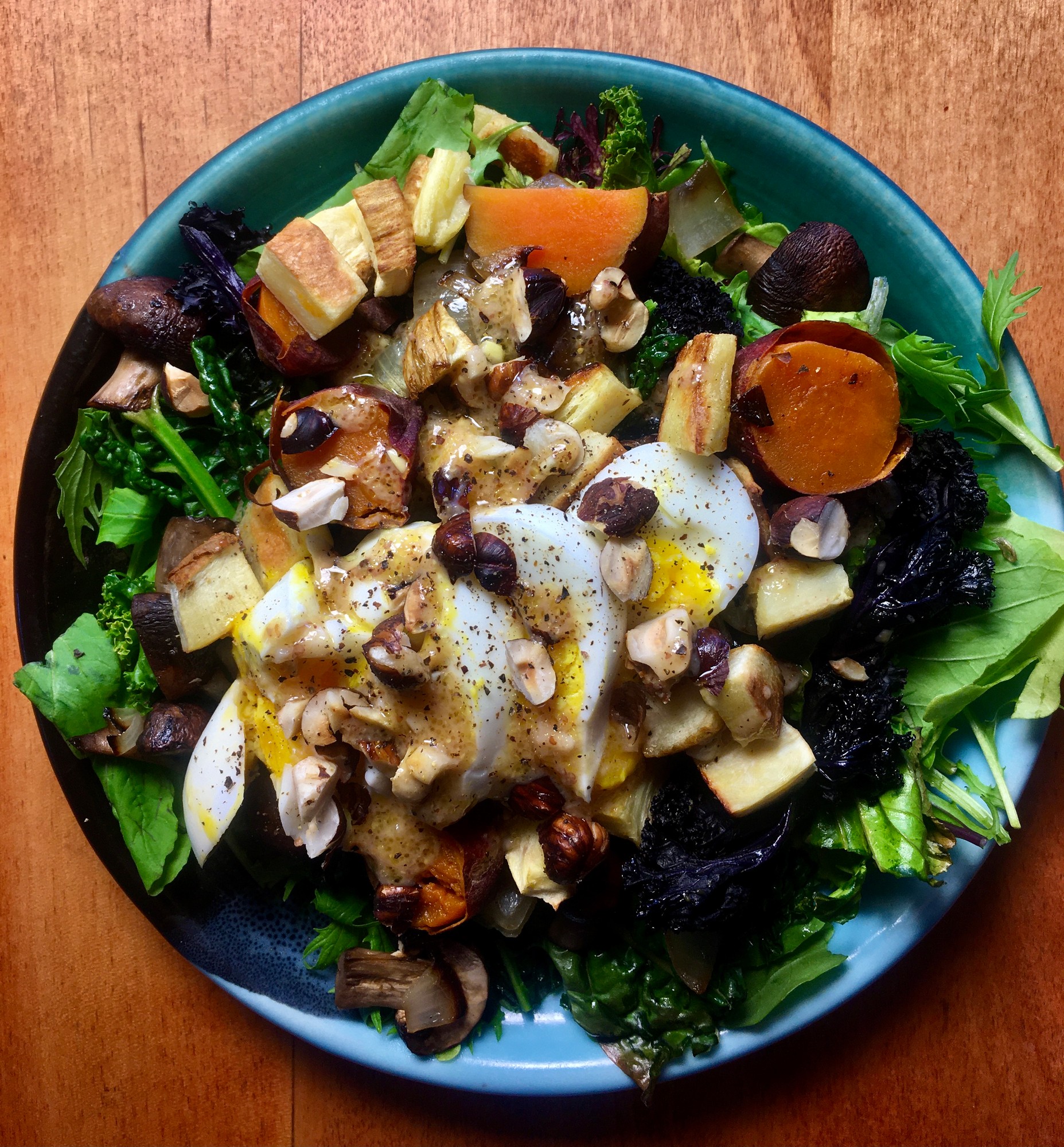 Roasted root vegetables, mushrooms and a sliced boiled egg on greens, topped with chopped nuts