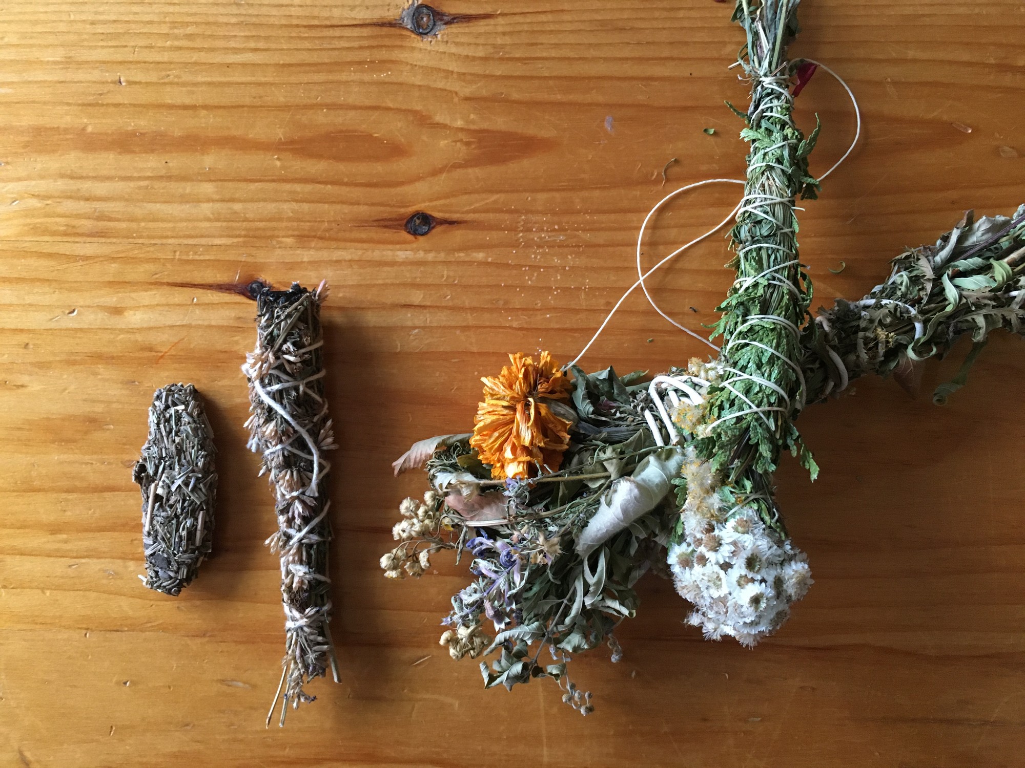 Bundles of dried herbs tied with white twine, one tucked with orange and white dried flowers, on a wooden table