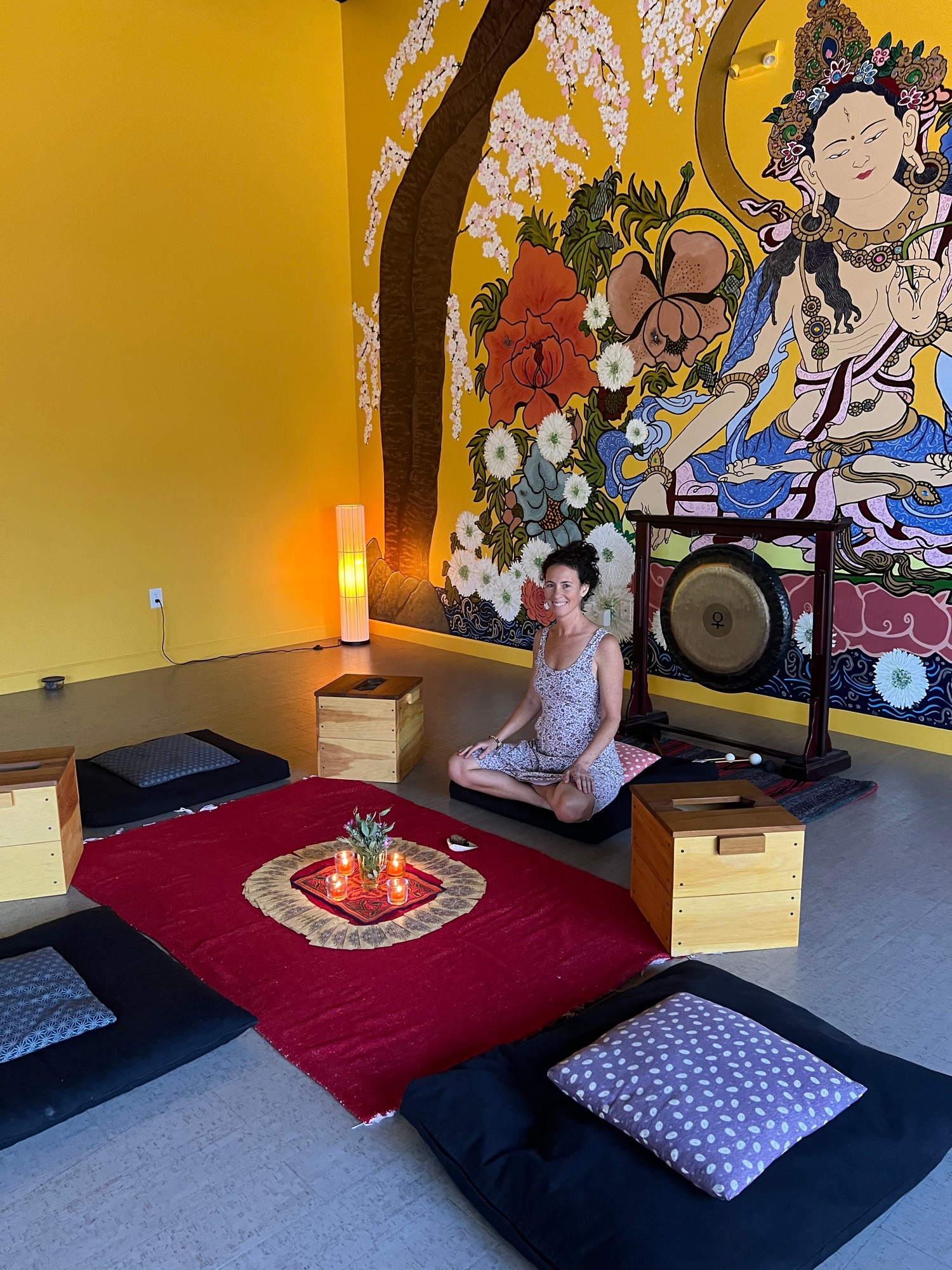 Vivian smiling beside a gong, steam boxes and cushions circled around candles