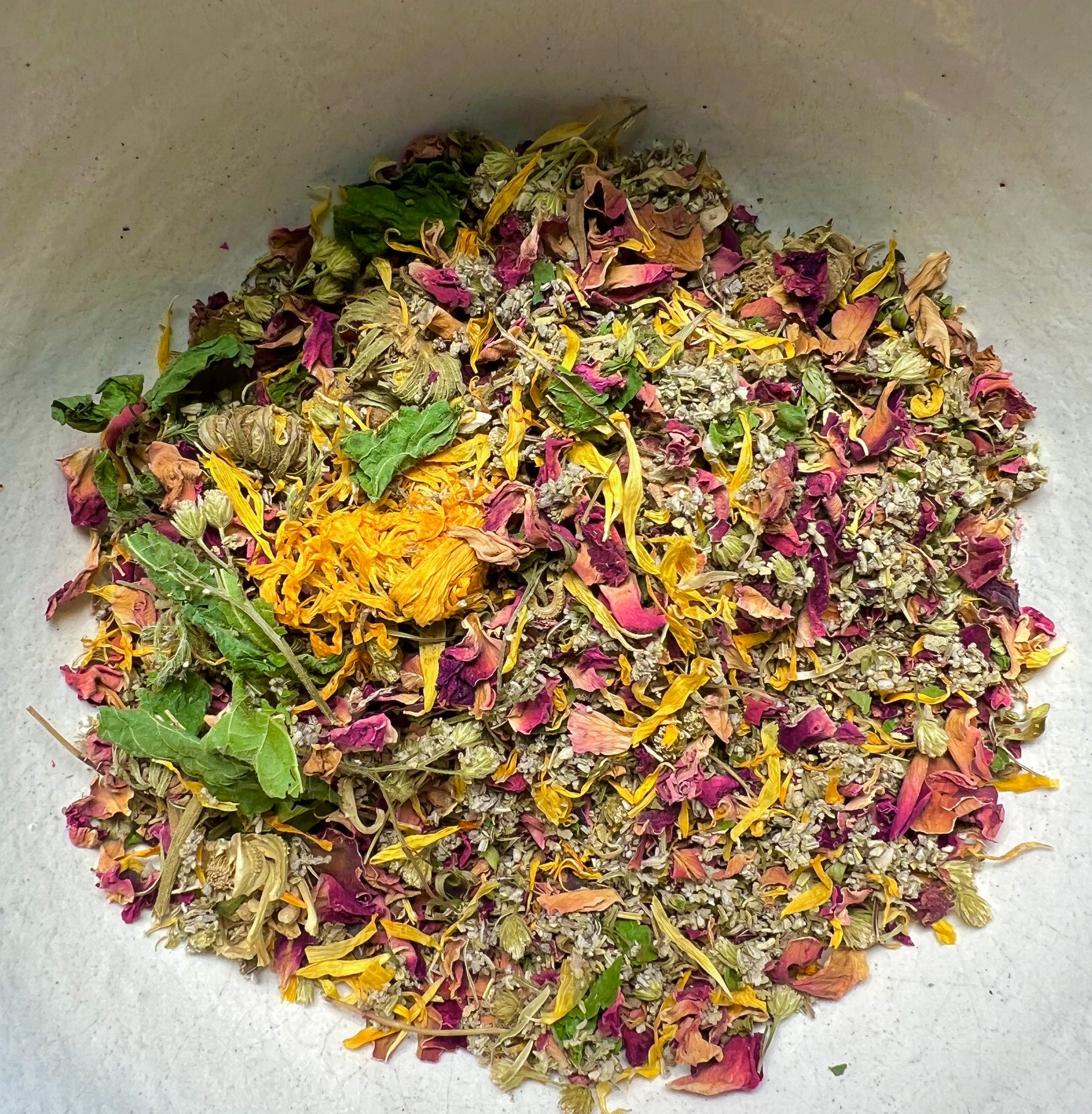 Dried rose petals, golden petals and green leaves heaped in a bowl
