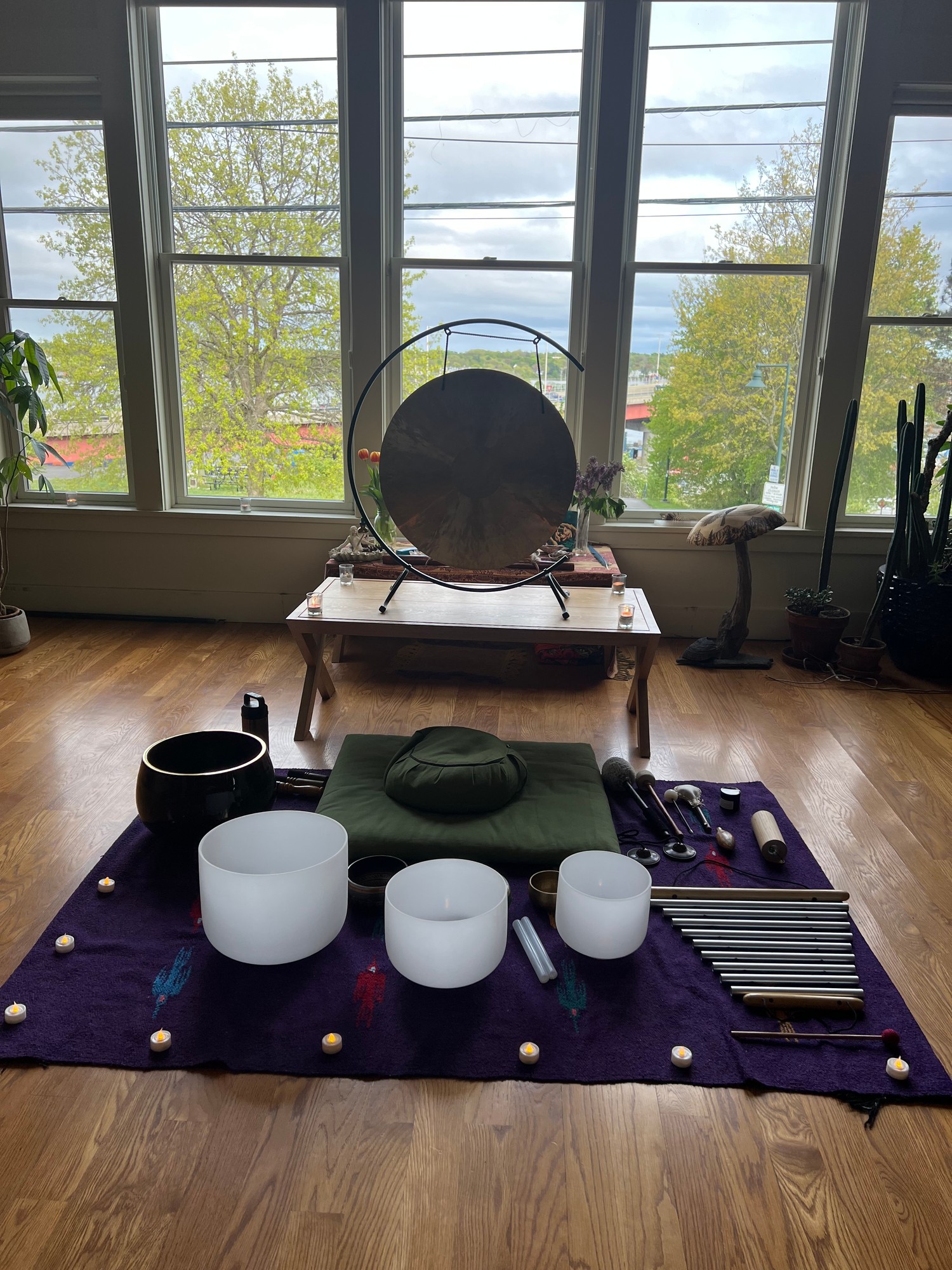 Gong before tall windows above crystal singing bowls, chimes and a cushion on a purple rug
