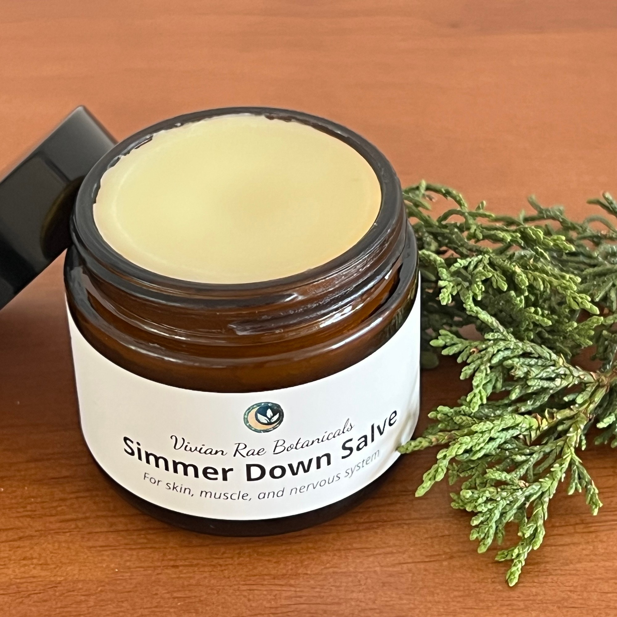 Open jar of Simmer Down Salve beside sprigs of alligator juniper