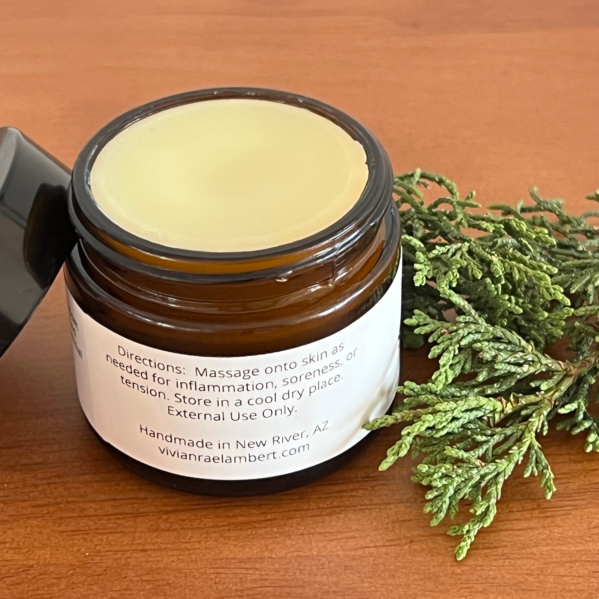 Open jar of Simmer Down Salve turned to its directions label, beside alligator juniper sprigs