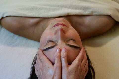 Hands gently cradling the face of a woman resting with eyes closed
