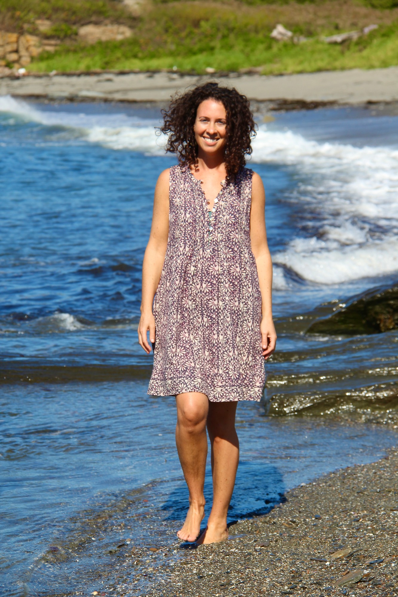 Vivian walking barefoot at the edge of a pebbly ocean shore