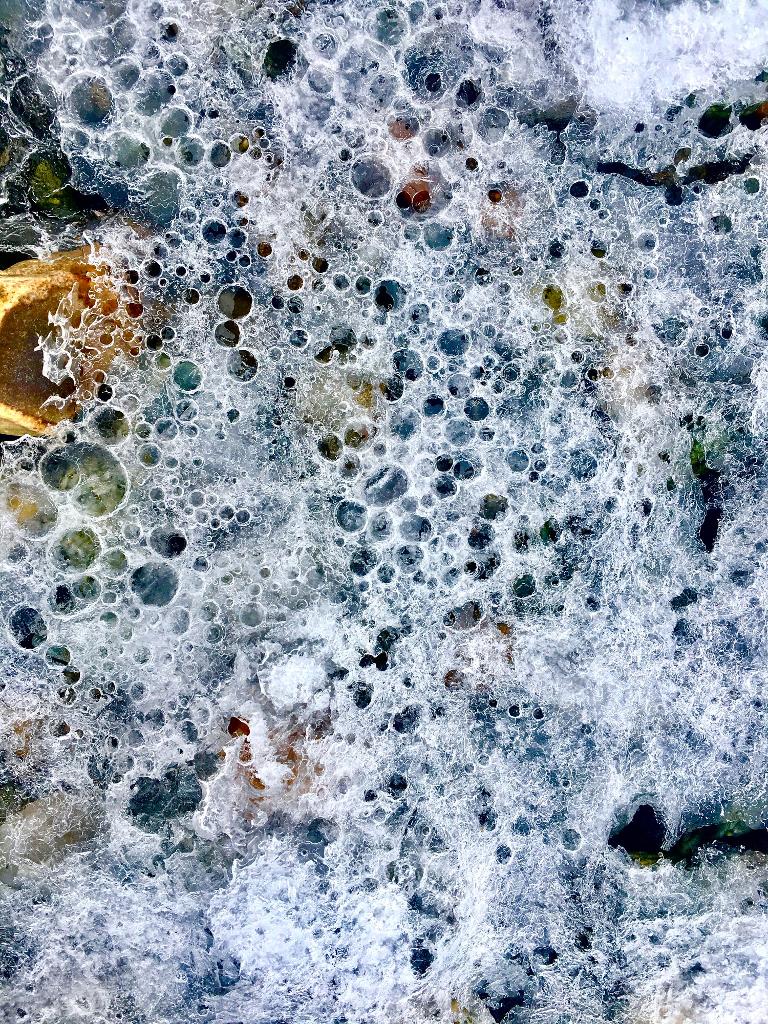 Lacy white froth and bubbles over pebbles in shallow water